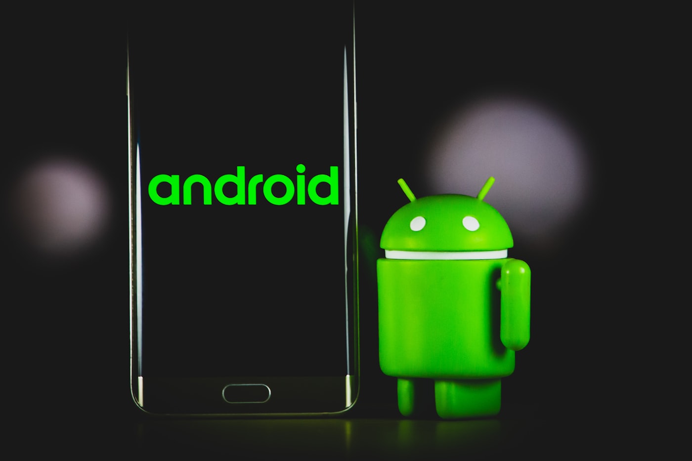Android smartphone glowing in a dark studio next to the Android mascot