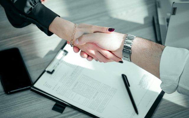 Handshake over a signed contract representing a fixed-price agreement