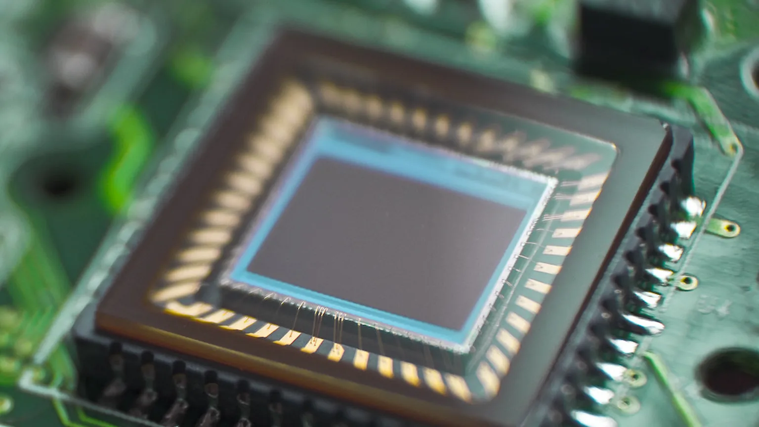 Extreme macro of a silicon chip die and gold bond wires on a green circuit board, representing the hardware that runs modern cryptography